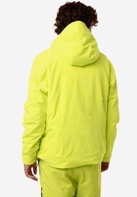 Giacca impermeabile gialla fluo con cappuccio e maniche lunghe. Texture liscia, progettata per la visibilità, con cuciture minime e vestibilità casual.