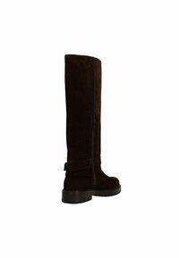 Botte en suedine marron jusqu'au genou avec une fermeture éclair sur le côté, bout rond et semelle en caoutchouc épaisse. Présente un détail de sangle enroulée. Design minimaliste.