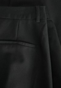 Zwarte op maat gemaakte broeken van een gladde stof, met een enkele achterzak, een vlakke voorkant en schone lijnen zonder zichtbare hardware.