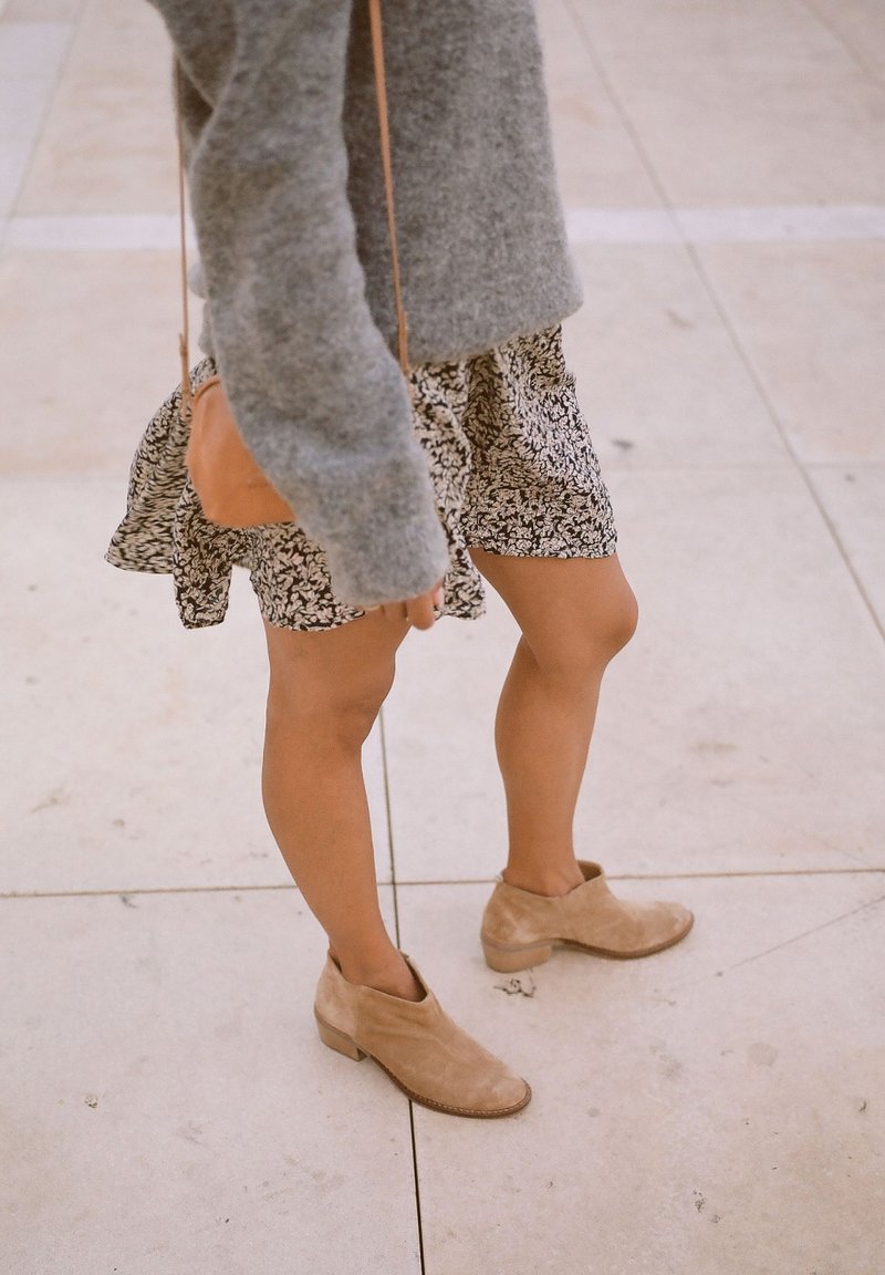 Suéter de punto gris, falda con estampado floral y botines tobilleros en color topo. El conjunto presenta un diseño casual con texturas suaves y colores naturales.