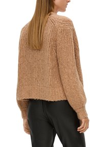 Strickpullover in einem hellbraunen Farbton mit lockerer Passform, ausgestattet mit gerippten Details und einem leicht verkürzten Saum, kombiniert mit schwarzen Hosen.