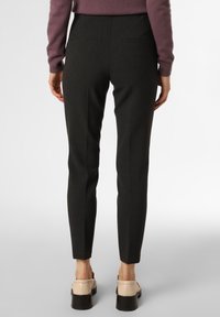 Pantaloni neri sartoriali con una vestibilità slim, due tasche posteriori e un tessuto leggermente testurizzato. Abbinati a scarpe beige con suola spessa.