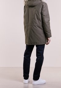 Parkа khaki z kapturem obszytym sztucznym futrem, o pikowanym wzorze, długości do połowy uda, z regulowanym sznurkiem w talii. Noszona z ciemnymi spodniami i białymi tenisówkami.