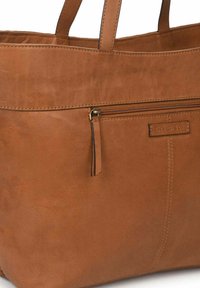 Bolso tote de cuero marrón con un bolsillo frontal con cremallera, acentos cosidos y dos asas cortas para un fácil transporte. Textura suave.