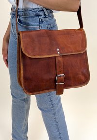 Borsa a tracolla in pelle marrone con parte anteriore piatta, dettagli cuciti, accessori in metallo argentato e tracolla regolabile. Finitura testurizzata.