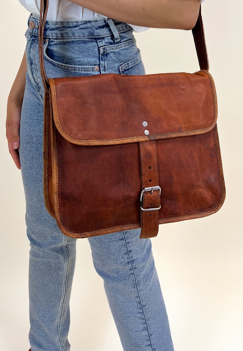 Borsa a tracolla in pelle marrone con parte anteriore piatta, dettagli cuciti, accessori in metallo argentato e tracolla regolabile. Finitura testurizzata.