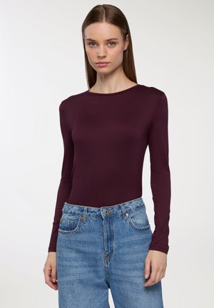 Top bordeaux a maniche lunghe con scollo rotondo, realizzato in tessuto morbido, abbinato a jeans in denim azzurro chiaro a vita alta.