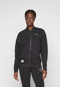 Sort zip-up sweatshirt med tekstureret stof, der har en stående krave, forlommer og en guld logo-accent på venstre bryst.