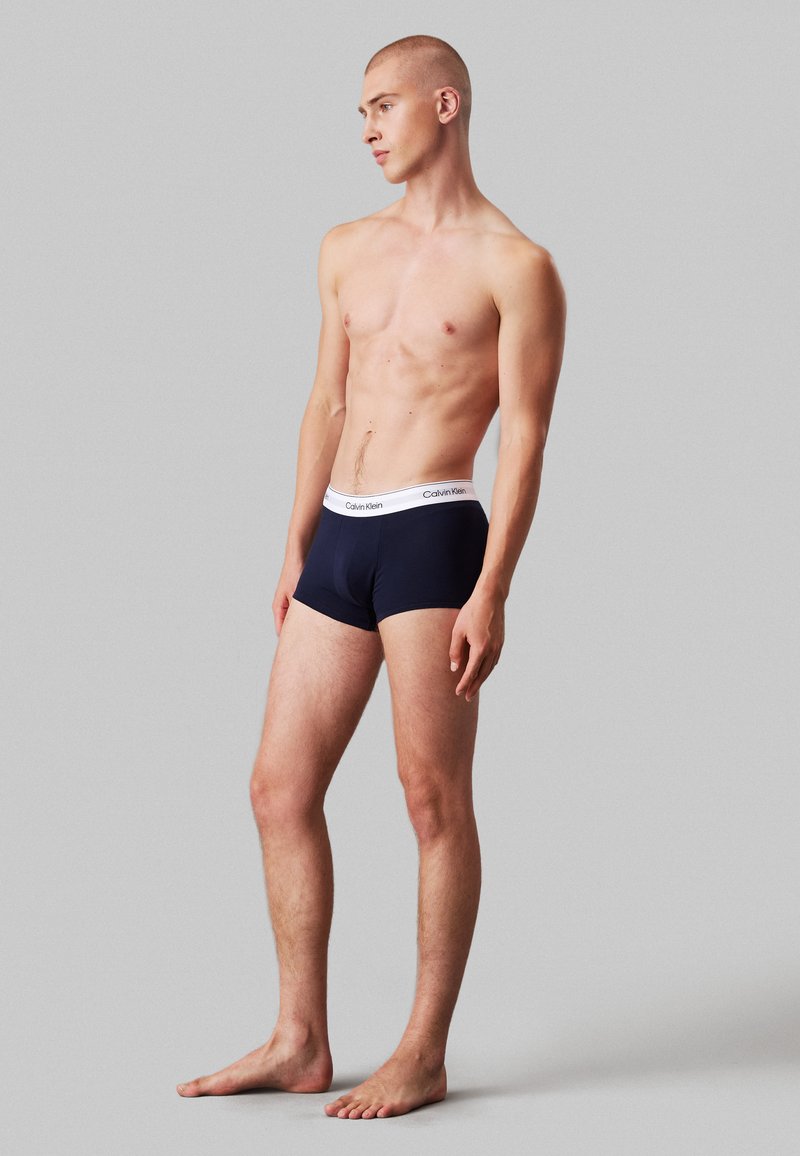 Marineblauwe katoenen boxershorts met een witte Calvin Klein-logo tailleband. Het ontwerp is aansluitend, soepel en heeft een middellange taille.