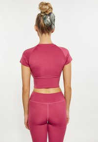 Rózsaszín aktív öltözék, amely rövid ujjú cropped felsőből és magas derekú leggingsből áll, sima, elasztikus anyagból készült.