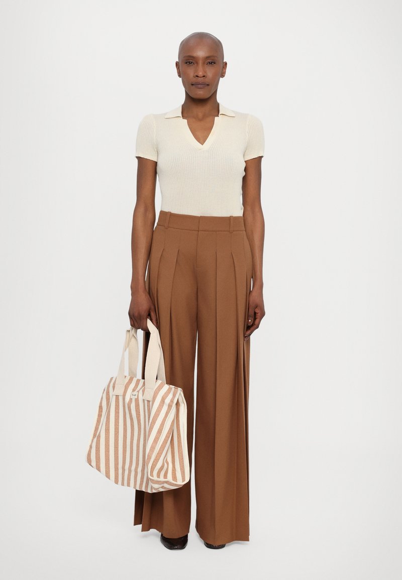 Cremefarbenes, geripptes Kurzarmoberteil, braune, hoch taillierte, plissierte Hose und eine gestreifte Tasche in Beige und Creme mit Canvasgriffen.