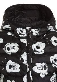 Czarna kurtka puchowa z białym wzorem kreskówkowej twarzy, posiadająca wysoki kołnierz, przedni zamek błyskawiczny oraz pikowany, przeszywany design.