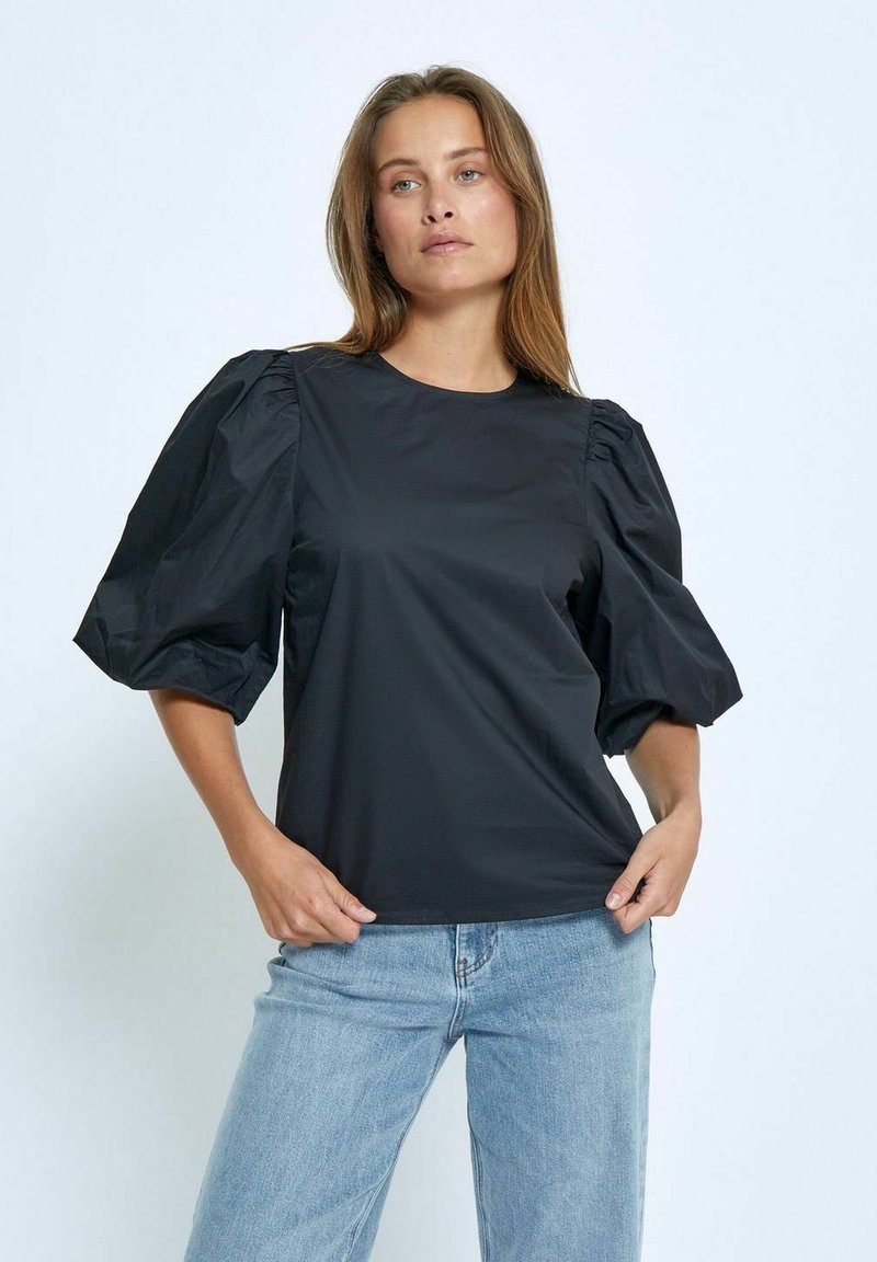 Top nero con maniche corte a sbuffo, realizzato in tessuto liscio; presenta un collo rotondo e una vestibilità rilassata. Indossato con jeans azzurri.