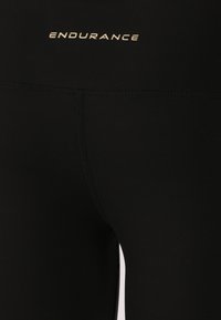 Zwarte legging van rekbaar materiaal, met een gouden "ENDURANCE" logo boven de taille en subtiele stikdetails.