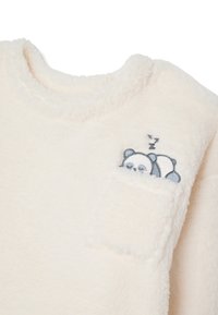 Suéter blanco y suave con un escote redondo y un bolsillo que presenta un panda durmiendo bordado. La tela es suave y tiene una apariencia texturizada.