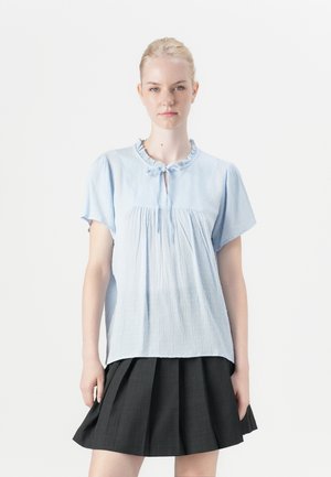 Lichtblauw kortmouwblouse met een gerimpelde halslijn, sleutelgatdetail en textuurstof. Gepaard met een donkere geplooide rok.