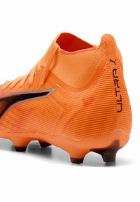 Lyse orange fodboldstøvle med en tekstureret overflade, sorte accenter og et højt krave-design. Har en syntetisk overdel og formede studs.