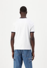 Camiseta de algodón blanca con cuello y acentos en las mangas de color azul marino, con un corte recto y mangas cortas.