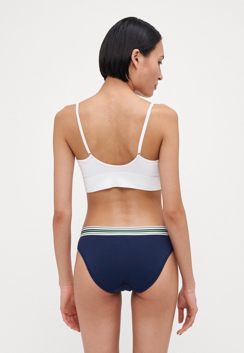 Bralette bianca con spalline sottili e una texture liscia, abbinata a slip blu navy con una vita a righe verde, bianca e blu navy.