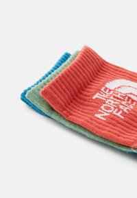 Drei Paar gestrickte Socken: ein leuchtend rotes Paar mit einem weißen Logo, ein grünes Paar und ein blaues Paar, die über gerippte Texturen und kontrastierende Farben verfügen.
