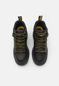 Svarta läderskor med gula accenter, rund tå, strukturerad yta och gröna samt gula snören. Har en dragflik på hälen.