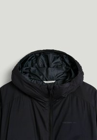 Sort hættejakke med polstret indvendig foret, lynlås foran og diskret "TRETORN 1891" branding på brystet.