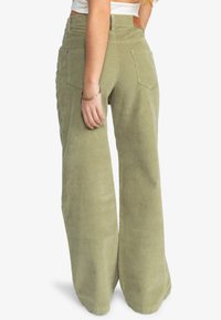 Brede corduroy broek in olijfgroen. Heeft een hoge taille, achterzakken en een textuurstof. Leren patchaccent op de tailleband.