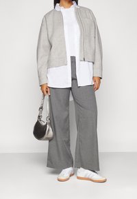 Grå, zip-up jacka över en vit skjorta, tillsammans med grå, vida byxor. Silverhandväska och vita sneakers med orange detaljer.