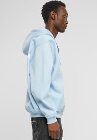 Hellblauer Hoodie mit einer Kordelzugkapuze, gerippten Bündchen und einer Fronttasche. Einfaches Design mit glatter Textur und minimalen Details.