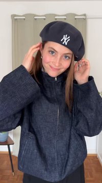 Sötét farmerdzseki magas gallérral és elöl cipzárral, fekete bőrrel párosítva, amelyen fehér Yankees-logó látható.