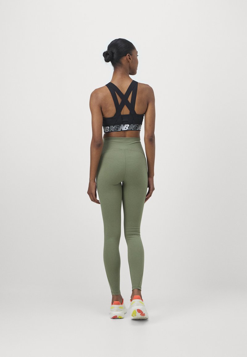 Sujetador deportivo negro con tirantes entrecruzados, leggings verdes de cintura alta y zapatillas blancas con detalles en naranja, vista desde la parte de atrás.