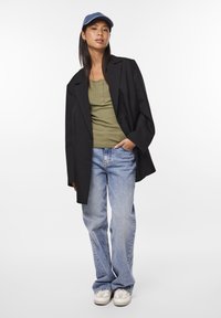 Sacou oversized negru, top din bumbac rib din olive verde, blugi flared de culoare albastru deschis, adidași albi și o șapcă din denim. Texturi netede, look casual.