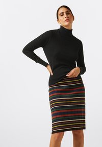 Zwarte coltrui met een gestructureerd patroon, gecombineerd met een rok tot de knie met multikleurige verticale strepen op een geribbelde stof.