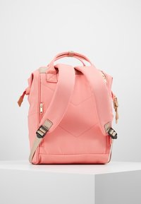 Růžový batoh s polstrovanými ramenními popruhy, pevně tvarovaný, diagonální prošívání a zlaté zipy jako ozdoby. Má boční kapsy na uložení.