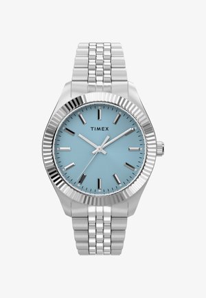 Sølvfarvet rustfrit stål Timex-armur med lyseblå urskive, sølvfarvede timeindikatorer og tre visere, der viser 10:09:35.