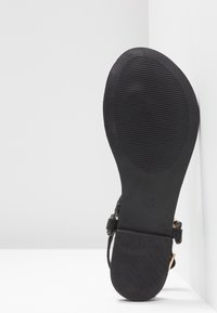 Black sandal sole showing a textured, flat rubber base with horizontal grooves, complemented by woven black straps and metallic accents.