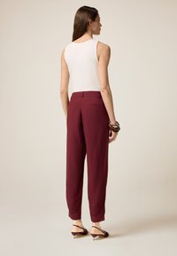 Pantaloni bordeaux a vita alta, morbidi al tatto, con tasche laterali e fondo affusolato, abbinati a un top bianco senza maniche.