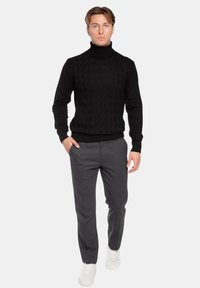 Maglione girocollo nero a treccia, abbinato a pantaloni grigi su misura e sneaker bianchi, che mette in risalto una silhouette aderente.
