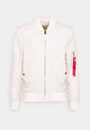 Lichtbeige bomberjack met een ritssluiting aan de voorkant, ribgebreide manchetten, twee zijzakken en een rode label op de linkermouw. Glad, licht glanzend stof.
