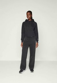 Felpa nera con cappuccio e coulisse, abbinata a pantaloni larghi coordinati. Il materiale sembra morbido, con un discreto dettaglio del marchio.
