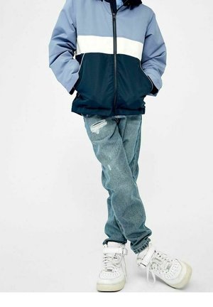 Blauw en marineblauw kleurgeblokkeerde jas met een ritsluiting, gecombineerd met lichtblauwe distressed jeans en witte hoge sneakers.