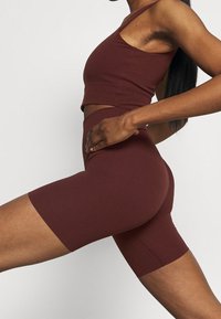 Burgundowy zestaw sportowy składający się z dopasowanej bezrękawnikowej bluzki oraz szortów z wysokim stanem. Wykonany z gładkiego materiału o bezszwowym designie.