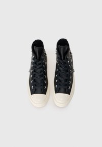 Vysoké tenisky s černým koženým svrškem, bílou gumovou špičkou a stříbrnými prvky, s tmavými tkaničkami a oky.