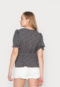 Blusa floral azul escura com mangas bufantes, cintura franzida e pequenas flores rosas e brancas; combinada com calções brancos desfiados.