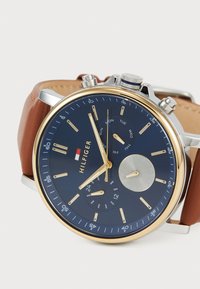 Montre avec bracelet en cuir marron, cadran bleu marine, accents en or et argent, sous-dials chronographe et affichage de la date.