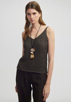 Débardeur en maille vert foncé avec un col en V, présentant de petites accents réfléchissants. Associé à un pantalon sombre, taille haute, marron foncé et un long collier.