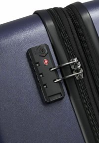 Valigia rigida blu navy con zip nera e lucchetto TSA. Le caratteristiche includono una superficie testurizzata e hardware argentato per una chiusura sicura.