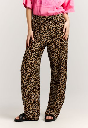 Wide-leg leopard print pants worn with pink graphic tee and black slide sandals, hands resting on hips.