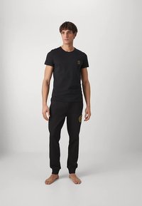 Μαύρο κοντομάνικο t-shirt με μικρό λογότυπο στο στήθος, συνδυασμένο με μαύρες φόρμες που διαθέτουν λεπτομέρεια λογότυπου στο μηρό.