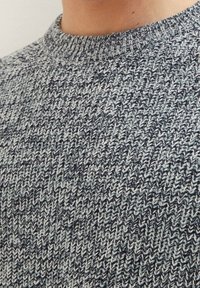 Close-up van een grijs en zwart gemarmerd gebreid sweater met een geribde ronde hals, gedragen door een persoon.